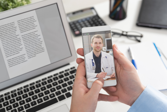 A male doctor is seen on the screen of a phone for a telehealth appointment. 