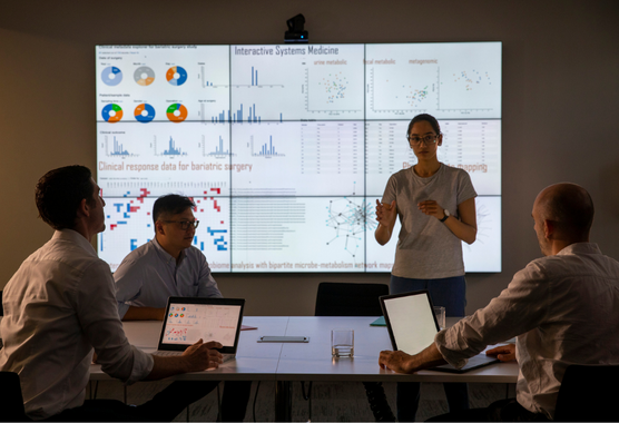 Group of people discuss data on a large screen. 