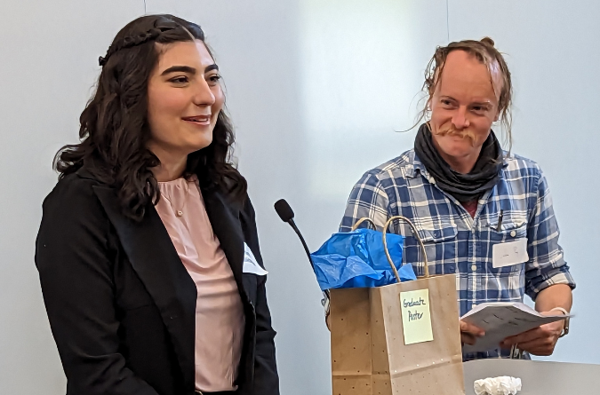 A woman in a dark dress coat accepts a student research award from UC Davis Prof. Jake Pry.