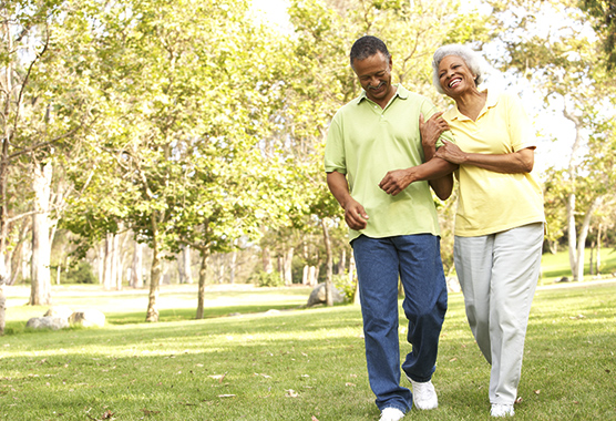 Older man walking with older woman on his arm smiling outside.