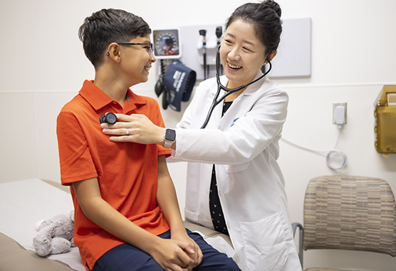 Female health care provider listening to young boy’s heart with a stethoscope.