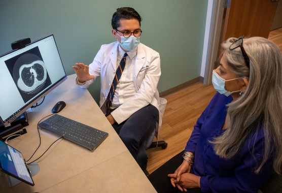 Male health care provider and female patient talking in front of a computer screen showing a lung scan