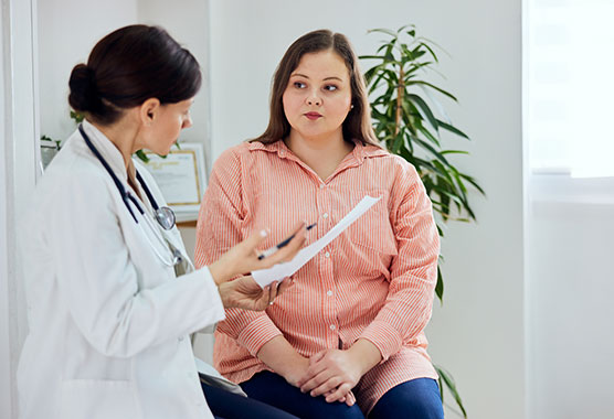 Woman sitting on exam table with female health care provider talking to her