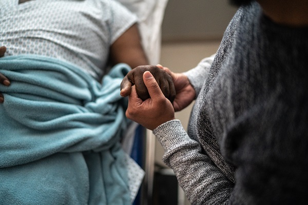 Patient in a hospital bed holding hands with a loved one.