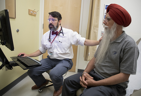 Male physician with his hand on male patient’s shoulder while looking at computer.