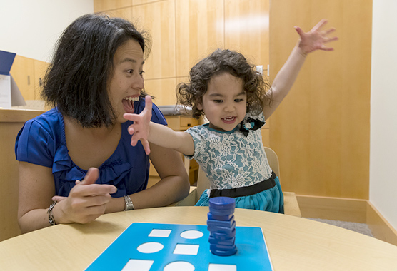 Mom and young girl smiling while playing with blocks on a table