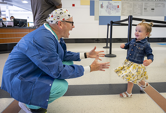 Smiling toddler running toward heart surgeon who is squatting with arms outstretched.