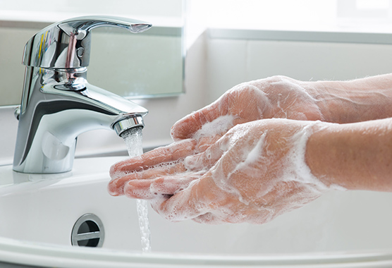 Hands with contact dermatitis being washed with soap and water under a sink.