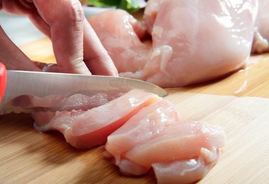 Person's hands cutting raw chicken on a cutting board.