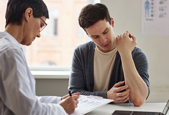 Man with eczema showing his dermatologist while sitting at a desk in clinic.