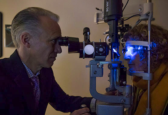A male health care provider examining a female patient’s eye in a dark room 