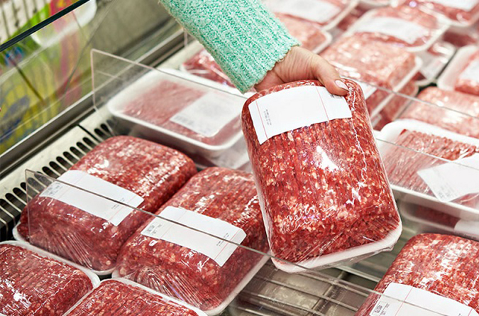 Ground beef packs in grocery store, with a woman’s hand reaching for a packet and picking it up.