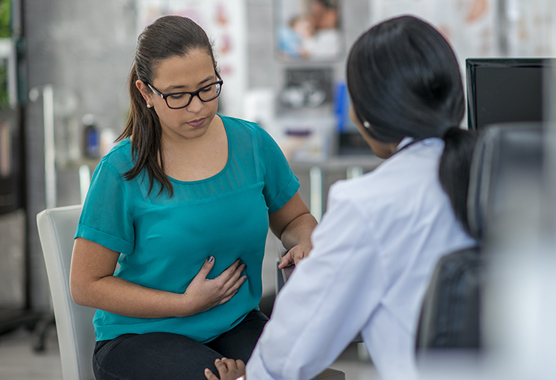 Woman holding her stomach while talking to health care provider.