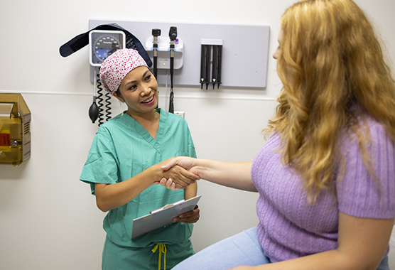 Woman sitting on an exam table shaking the hand of her female health care provider.