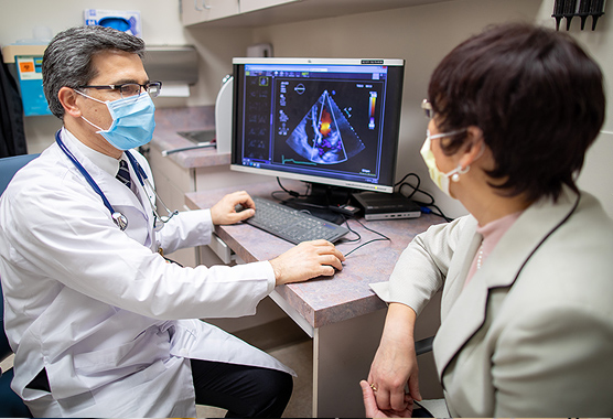 Masked male physician looks at scans with an older female patient