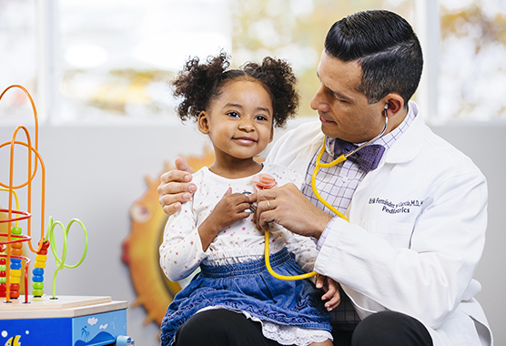 Young girl smiling sitting with male health care provider who is listening to her heart with a stethoscope.