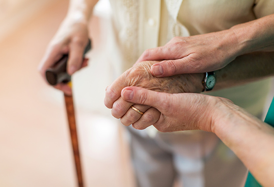 Older person with a cane holding hands with a younger person.