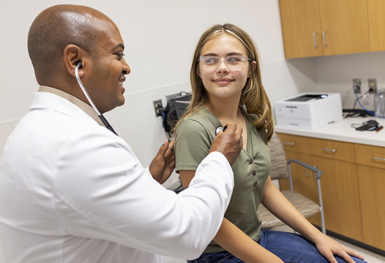 Male health care provider listening to girl’s heart with stethoscope.