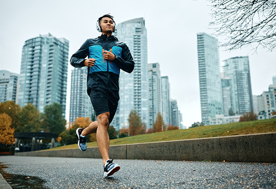 A man wearing headphones runs on a path in a city.