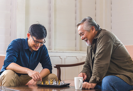 Older man and younger man sitting around a table playing chess