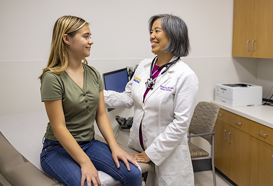 A female physician and young female patient in an exam room smiling at each other.