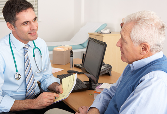 Male physician talking with older male patient about movement disorders.