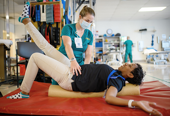 Female physical therapist with her hands on female patient’s hips as they do an exercise with the patient laying on her back.
