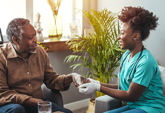 Female health care provider holding the hand of older man with Parkinson’s disease as both are smiling.