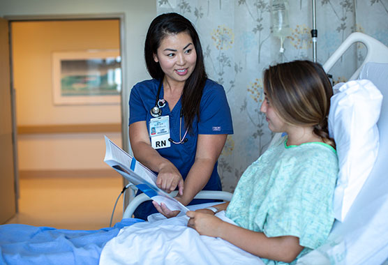 Smiling female nurse showing papers to female patient in a hospital bed  