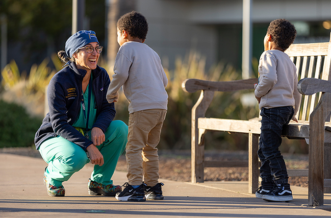 Two young boys talking to a female health care provider outside next to a bench.