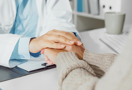 Health care provider’s hands holding patient's hands on a desk.