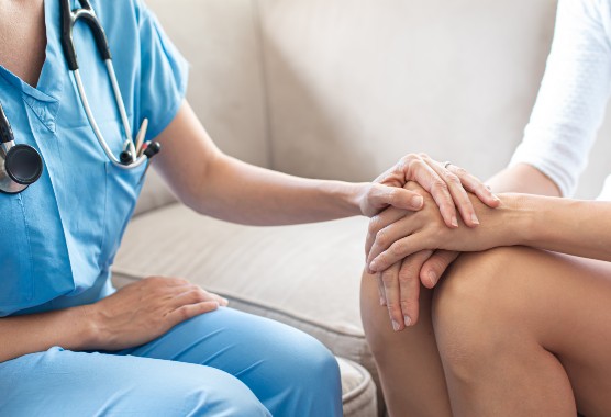 Female health care provider sitting with her hand on female patient’s hands