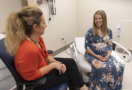 Pregnant woman smiling at her provider in an exam room.