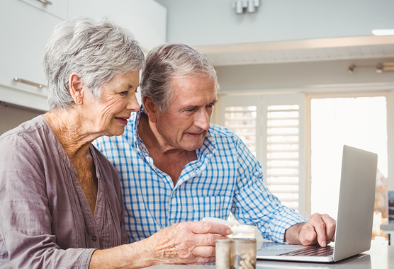 Older man and woman researching on a laptop in their kitchen.