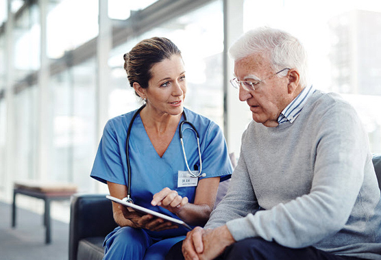 Mature male patient sitting next to his female health care provider who is showing him something on a tablet 