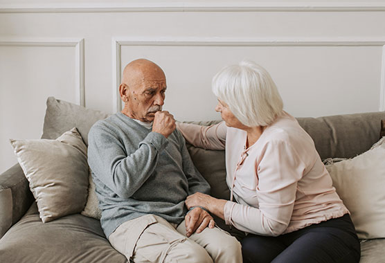 Older man coughing while older woman sits next to him seeing what's wrong