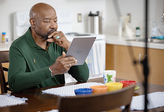 Man looking serious as he reads a mobile tablet at a kitchen table.
