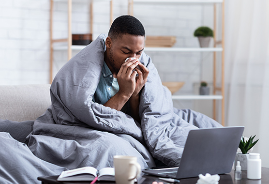 Man with sinus infection sitting in bed blowing his nose.