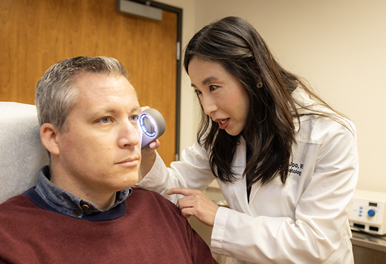 A dermatologist uses a dermatoscope on a male patient.
