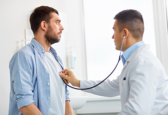 Male health care provider listening to the heart of a man with a stethoscope.