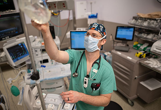 Male anesthesiologist adjusting an IV bag in an operating room 