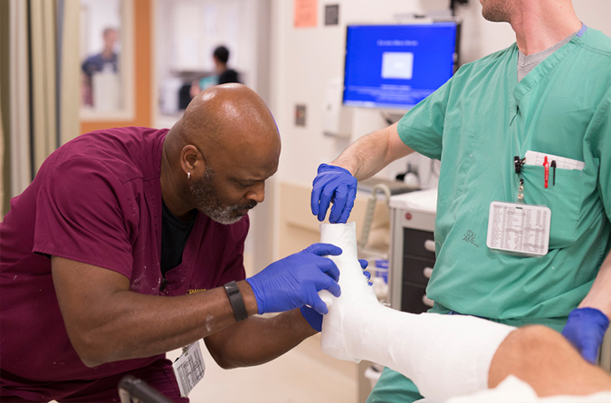 Two medical providers putting gauze on a patient’s leg in preparation for a hard cast.