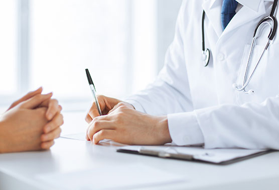 Close-up of medical professional's hands writing while patient's hands are resting across on a table