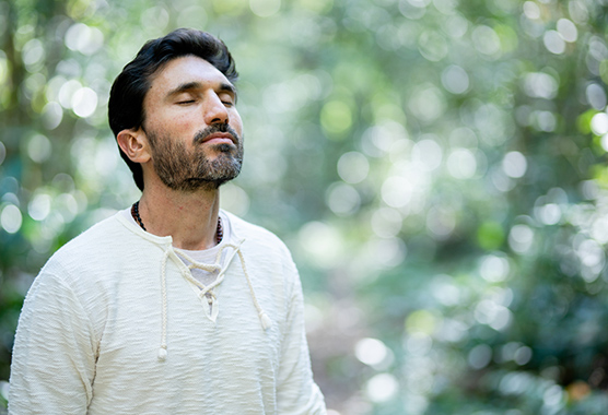 Man taking a deep breath as he stands alone in a forest.