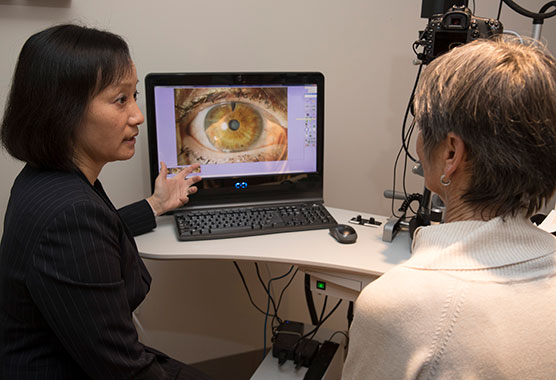 Eye physician and female patient in an exam room looking at an image of an eye on a computer screen