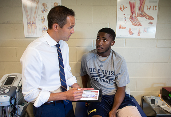 Physician talking to a UC Davis football player about injury prevention in a clinic.