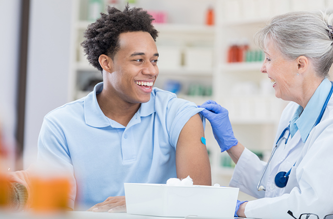 Younger man smiling at health care provider after getting vaccine in his arm.