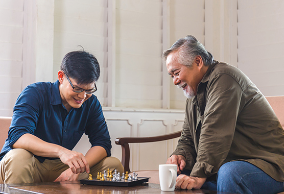 Older man and younger man sitting around a table playing chess.