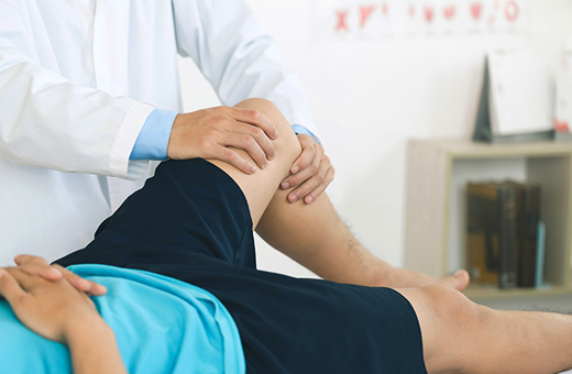 A physical therpaist bends and supports a patient’s leg.