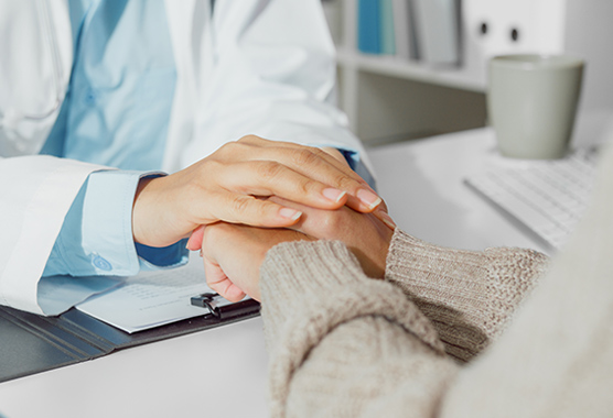 Health care provider holding the hands in a caring manner of a patient at a desk.